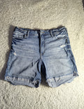 Light wash blue denim shorts with distressed details and raw frayed hems, laid flat on a textured gray carpet.