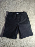 Black denim shorts laid flat on a textured beige carpet, with a visible waistband and front pocket.
