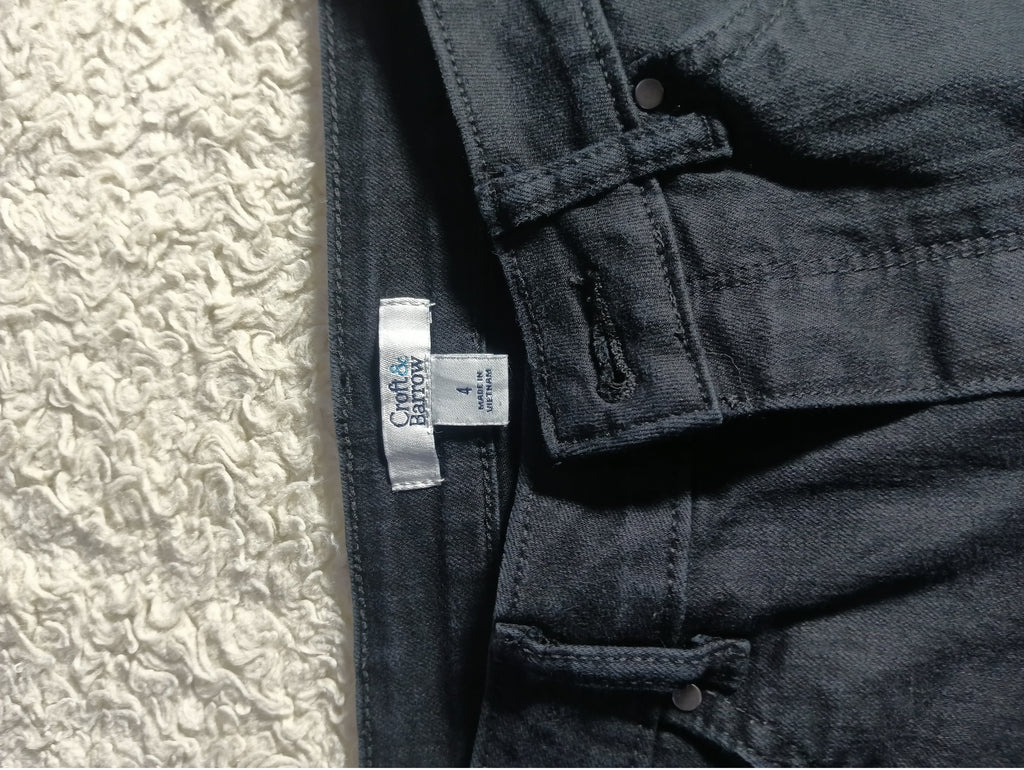 Close-up of dark charcoal gray denim jeans showing the inner waistband, button closure, and a white sewn-in size label that reads 'CULT OF LONDON'.
