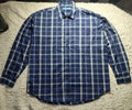 A blue and white plaid long-sleeve button-up shirt laid flat on a white shag rug.