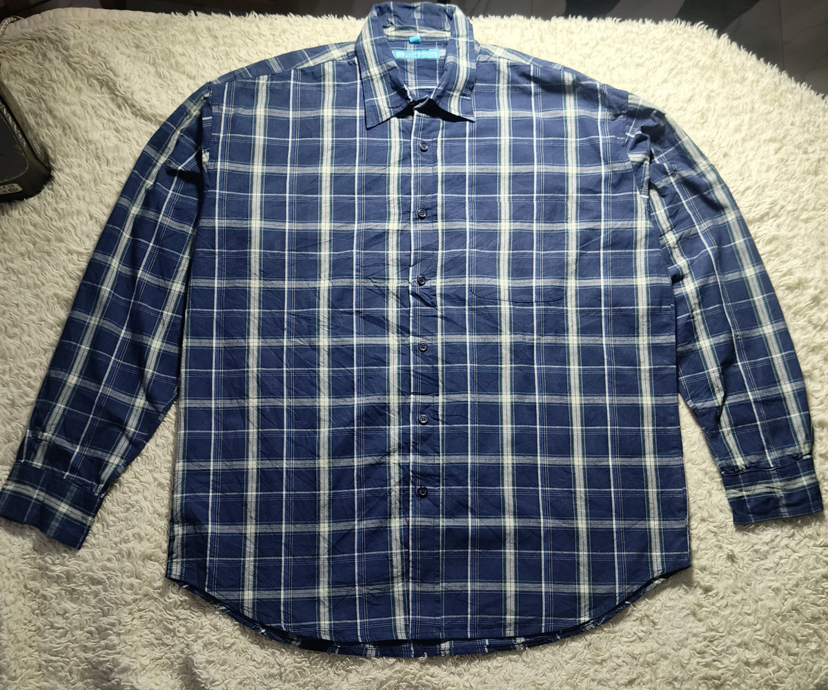 A blue and white plaid long-sleeve button-up shirt laid flat on a white shag rug.