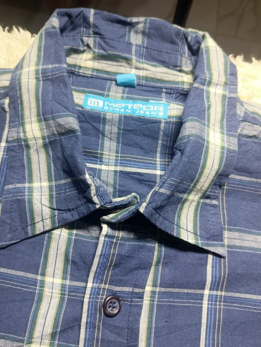 A close-up of a blue plaid button-up shirt with white and green stripes, showing the collar and inner label which reads 'Meteor Jordan Jeans'.