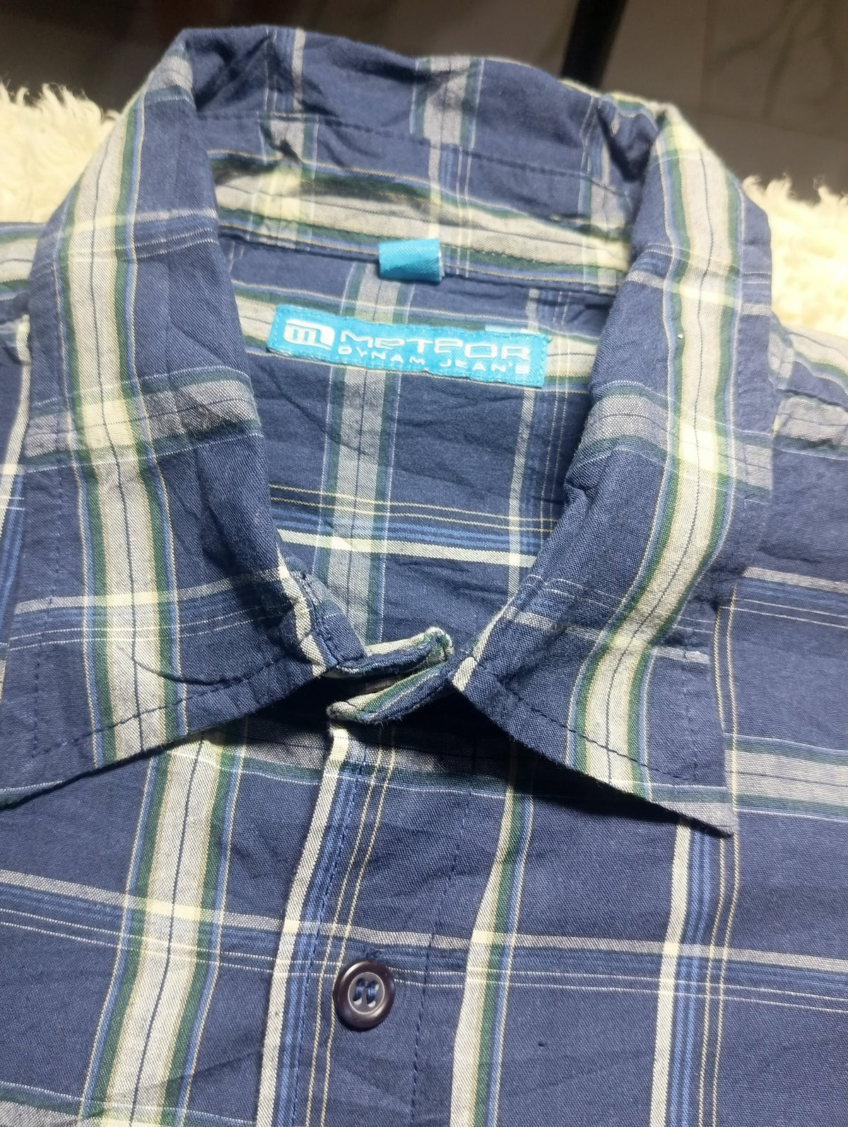 A close-up of a blue plaid button-up shirt with white and green stripes, showing the collar and inner label which reads 'Meteor Jordan Jeans'.