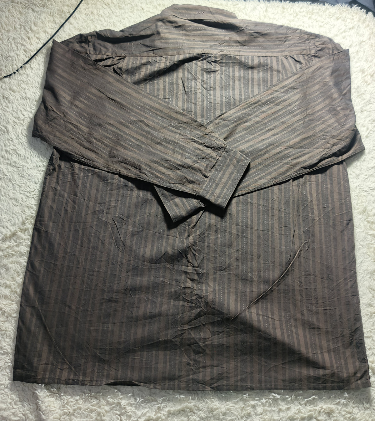 A brown and black vertically striped long-sleeve button-up shirt laid flat on a white textured rug.