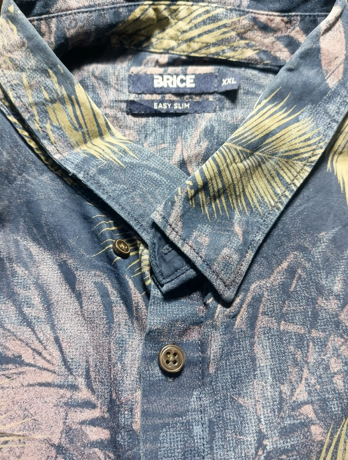 Close-up of a collared button-up shirt by The BRICE, featuring a blue-gray base with a yellow palm leaf print and a visible 'EASY JUMPER' label.