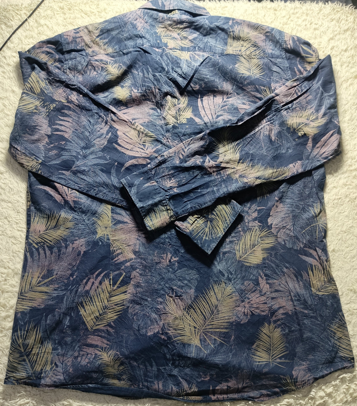 A long-sleeve button-up shirt with a tropical palm leaf pattern in navy blue, dusty pink, and beige, laid flat on a white textured carpet.