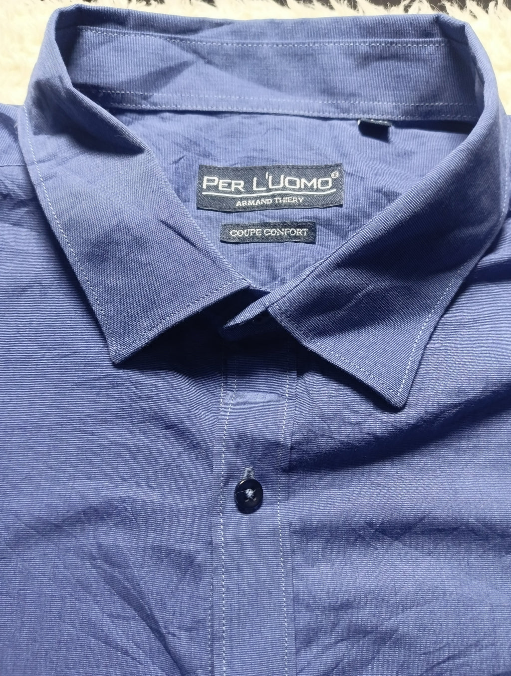Close-up of a blue long-sleeve button-down shirt collar with the brand label 'PER L'UOMO' visible inside the neck.