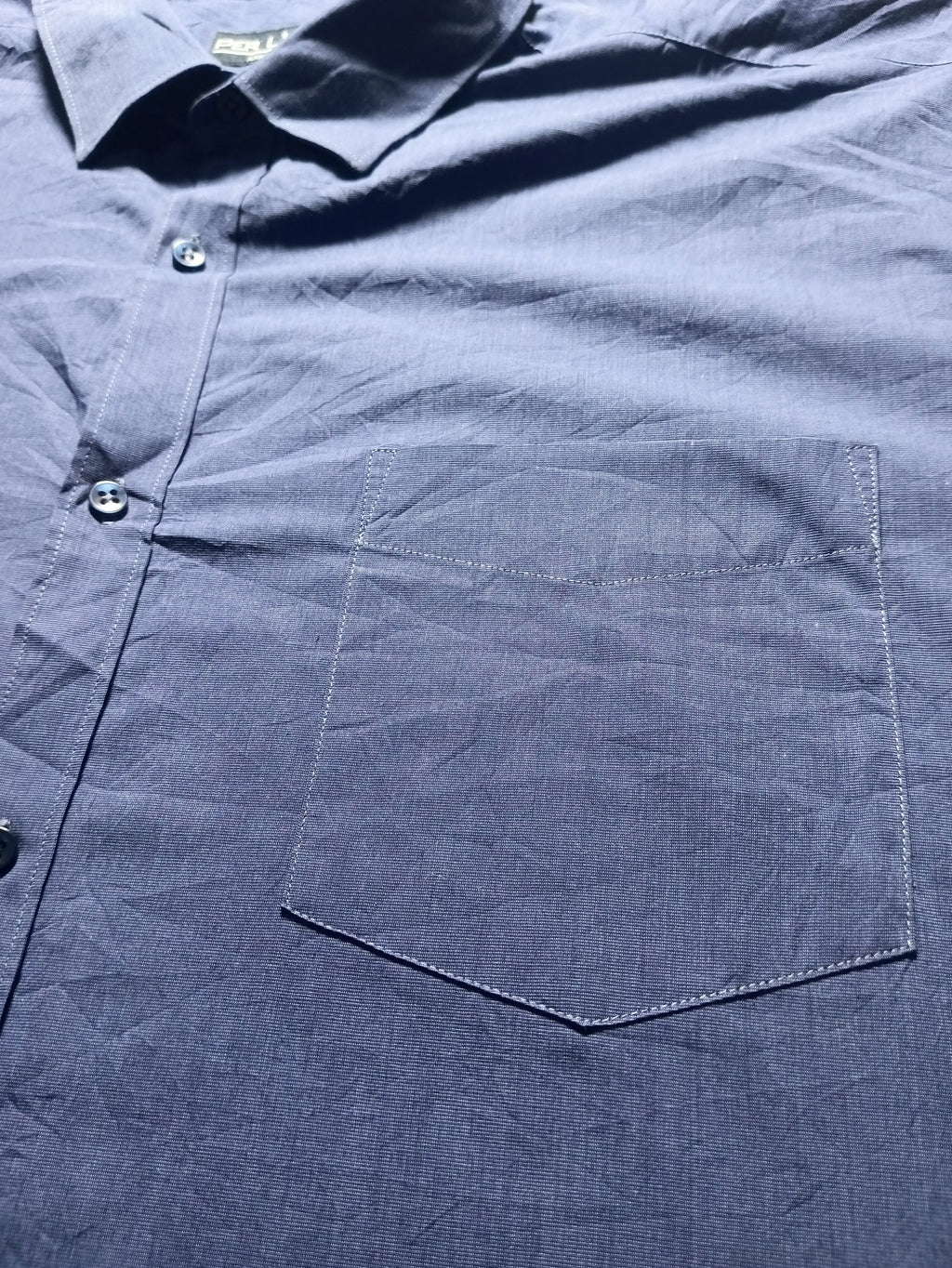A close-up of a dark navy blue button-down shirt showing the chest pocket, collar, and fabric texture.