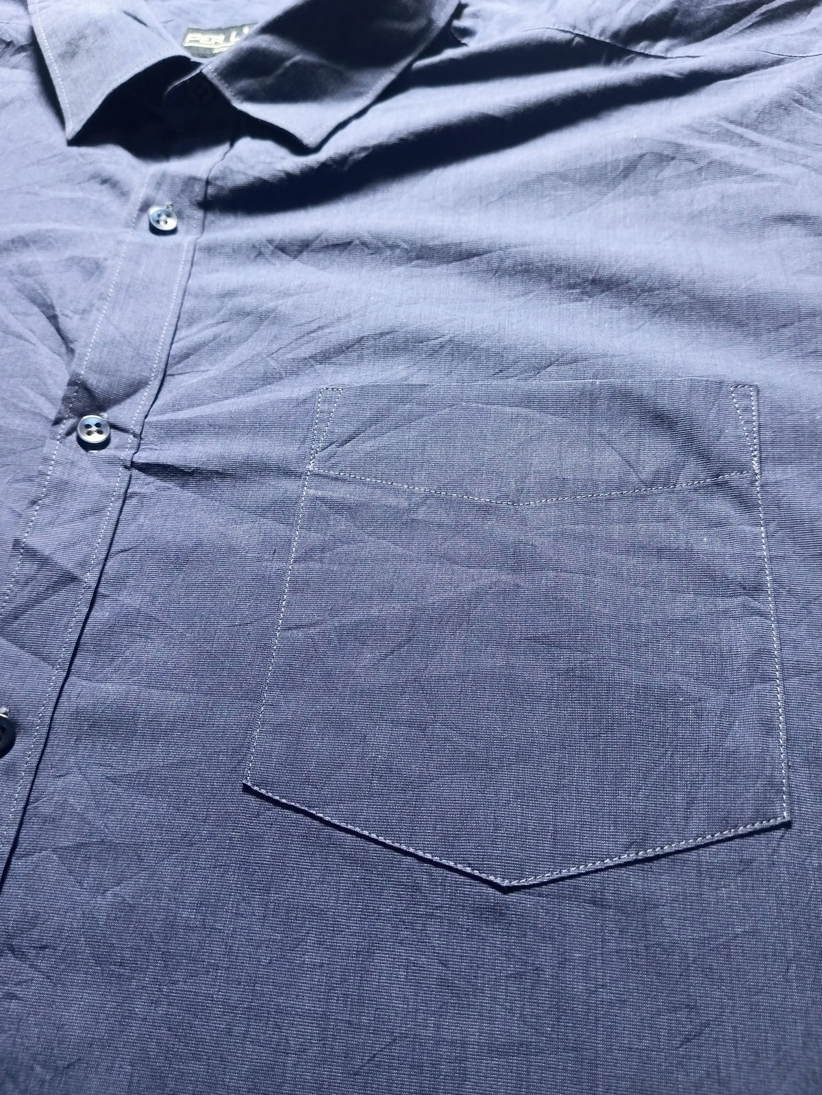 A close-up of a dark navy blue button-down shirt showing the chest pocket, collar, and fabric texture.