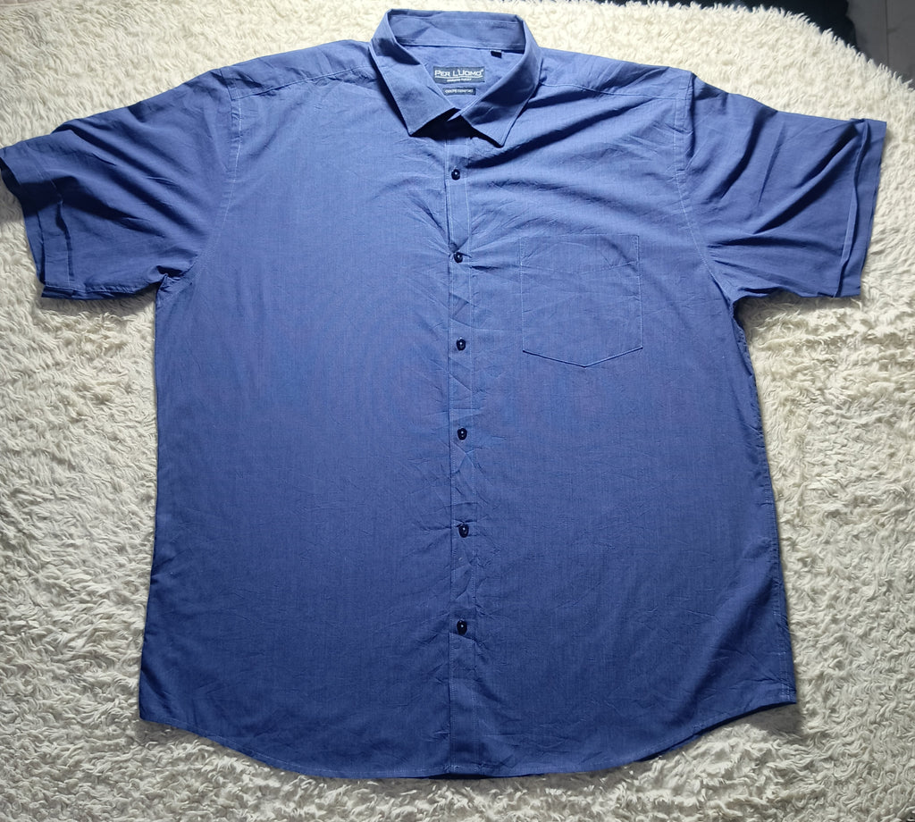 A blue short-sleeve button-up shirt laid flat on a white shag rug. The shirt has a pointed collar, a left chest pocket, and dark buttons down the front.