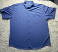 A blue short-sleeve button-up shirt laid flat on a white shag rug. The shirt has a pointed collar, a left chest pocket, and dark buttons down the front.