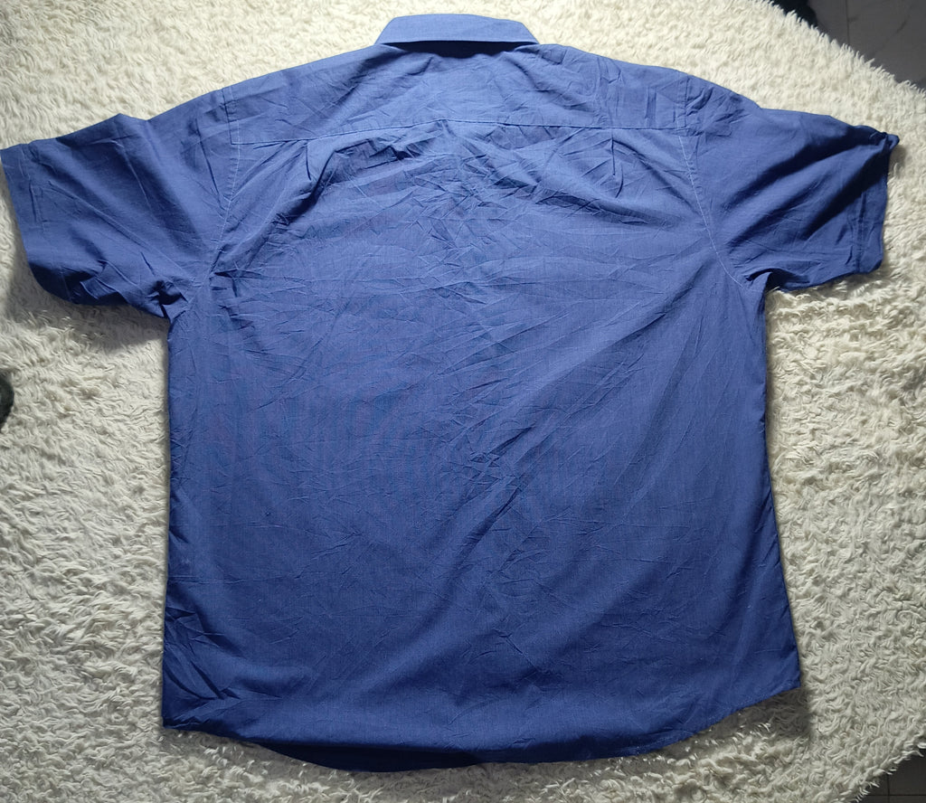 A blue short-sleeve button-up shirt laid flat on a white shag rug, showing the back side of the garment.