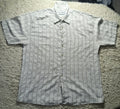 A short-sleeve button-up shirt with a fine vertical stripe pattern in gray and white, laid flat on a textured beige shag rug. The brand name 'SOLIS' is visible on the inner neck label.