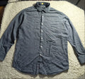 A long-sleeve button-up shirt in a faded blue-gray color, laid flat on a white shaggy blanket in a home setting.
