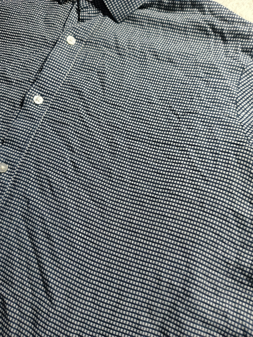 Close-up of a black and white micro-patterned button-down shirt, showing the fine striped weave and white buttons.