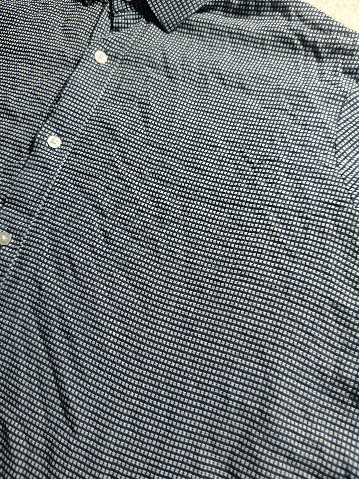 Close-up of a black and white micro-patterned button-down shirt, showing the fine striped weave and white buttons.