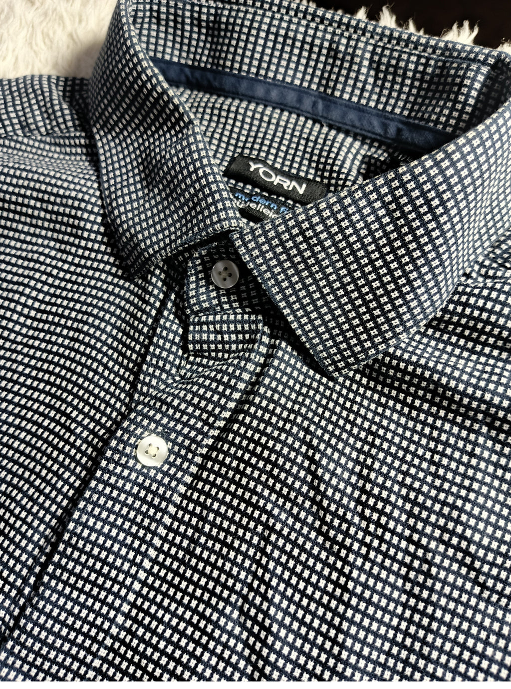 Close-up of a POVA Neo button-down shirt featuring a dense micro-checkered pattern in black and white, with a visible collar and button.