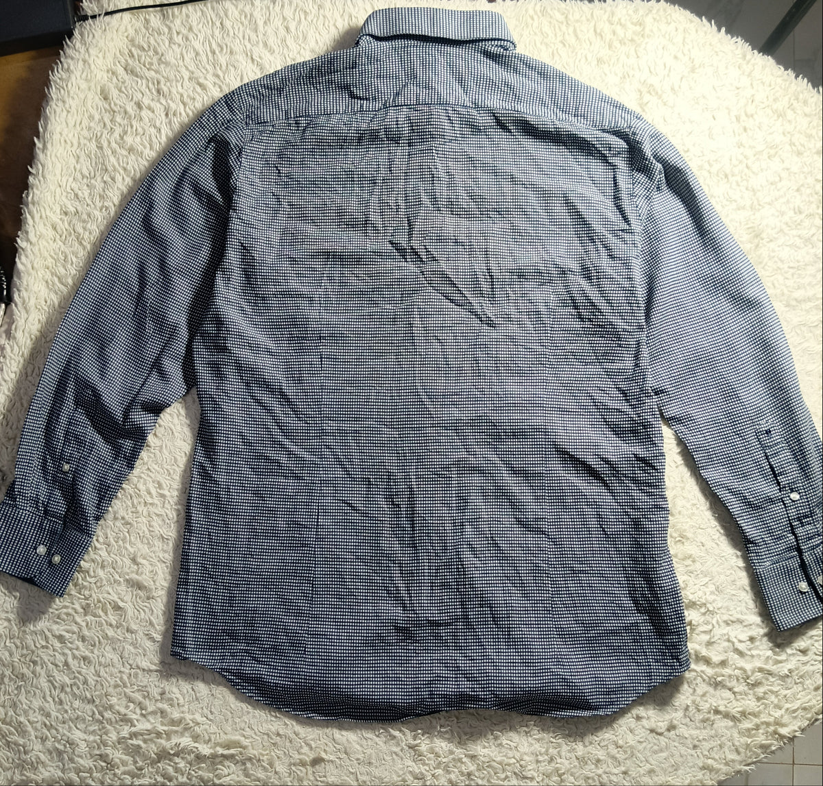 A long-sleeve gray button-up shirt laid flat on a white shaggy blanket, photographed from above in a casual indoor setting.