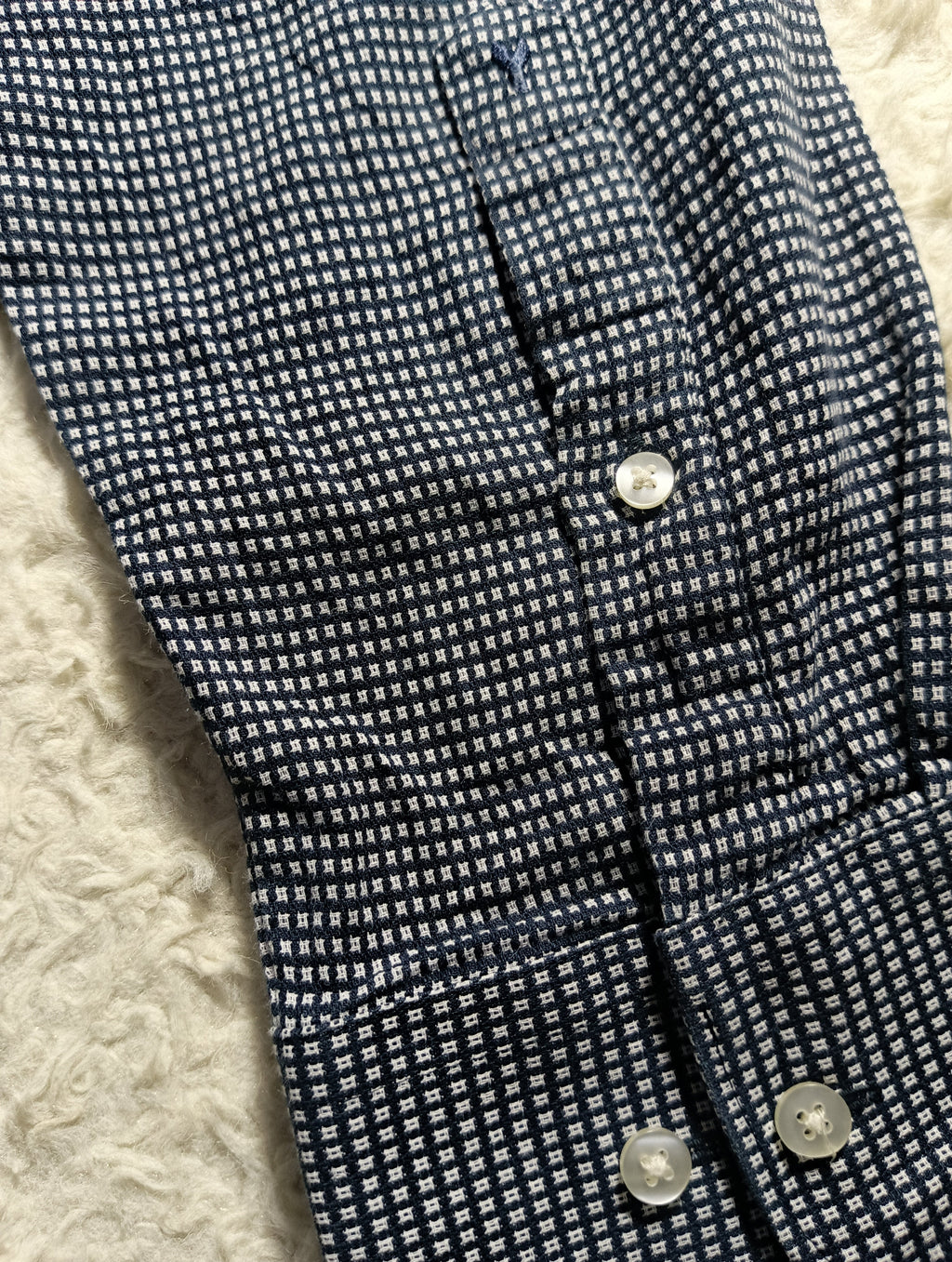 Close-up of a navy and white micro-check patterned fabric, likely a shirt or jacket lining, with visible buttons and a textured cream surface underneath.