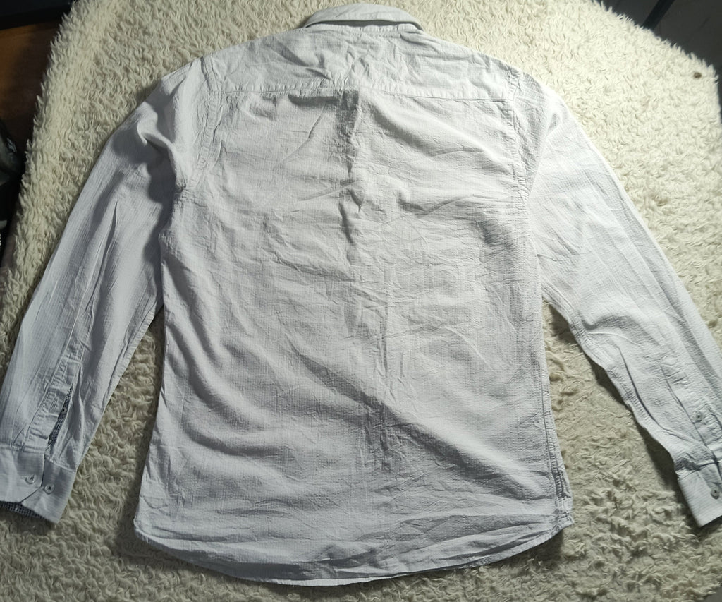 A light gray long-sleeve button-up shirt laid flat on a white shaggy blanket, photographed in a casual indoor setting.