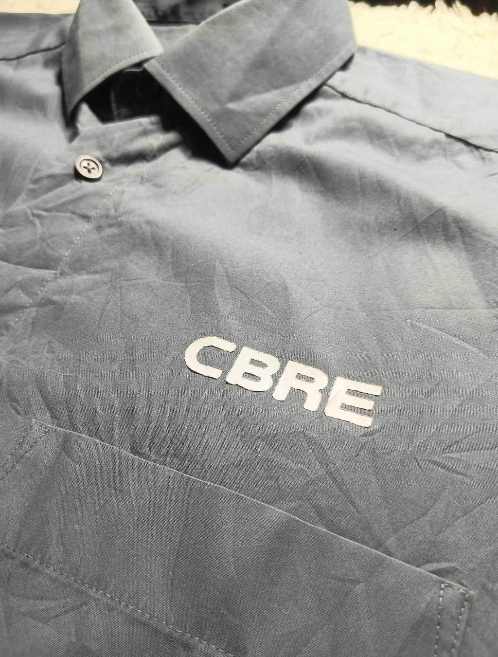 A close-up of a dark gray collared shirt with 'CBRE' embroidered in white on the chest, laid flat.
