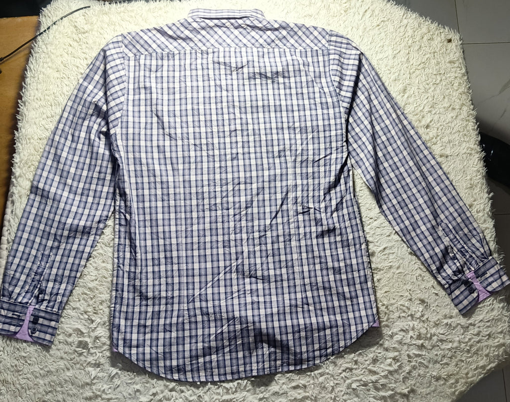 A long-sleeve button-up shirt with a blue and white checkered pattern, laid flat on a white shag rug.