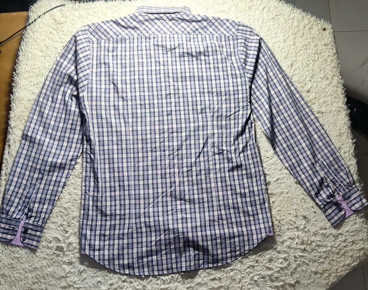 A long-sleeve button-up shirt with a blue and white checkered pattern, laid flat on a white shag rug.
