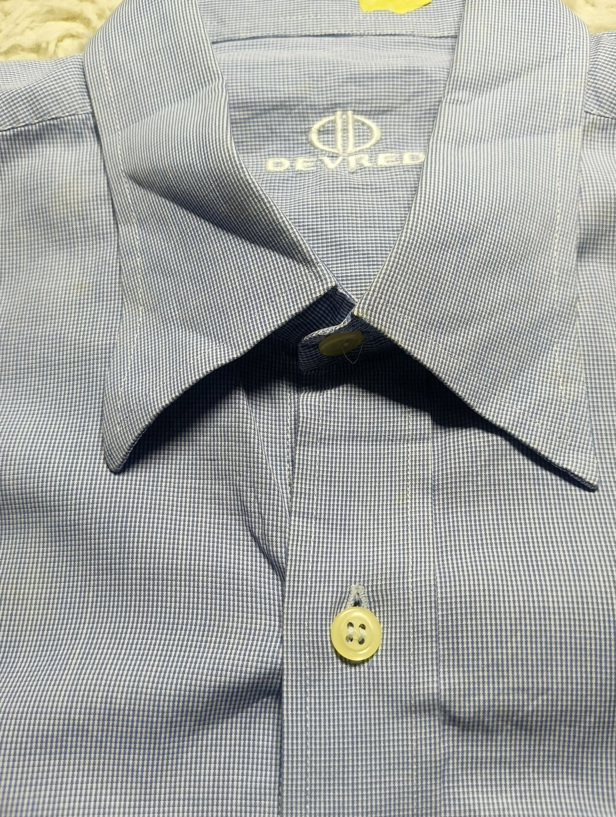 Close-up of a Devred men's dress shirt featuring a fine blue and white micro-check pattern, a classic collar, and a single light-colored button.