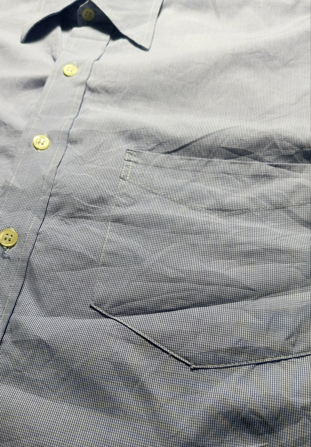 Close-up of a gray micro-check button-down shirt with yellow buttons and a chest pocket, photographed in detail.