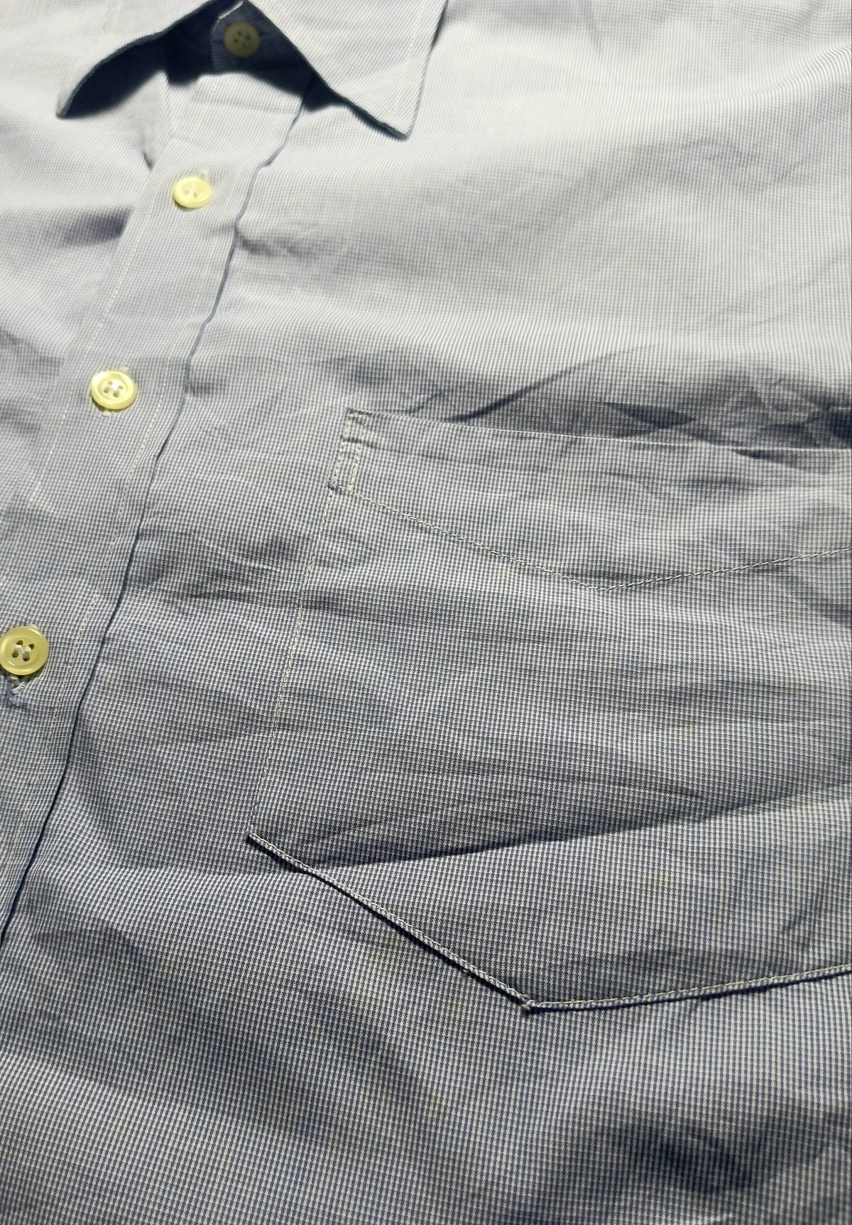 Close-up of a gray micro-check button-down shirt with yellow buttons and a chest pocket, photographed in detail.