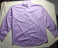 A light purple long-sleeve button-up shirt laid flat on a white shaggy blanket, with a tiled floor and dark furniture visible in the background.