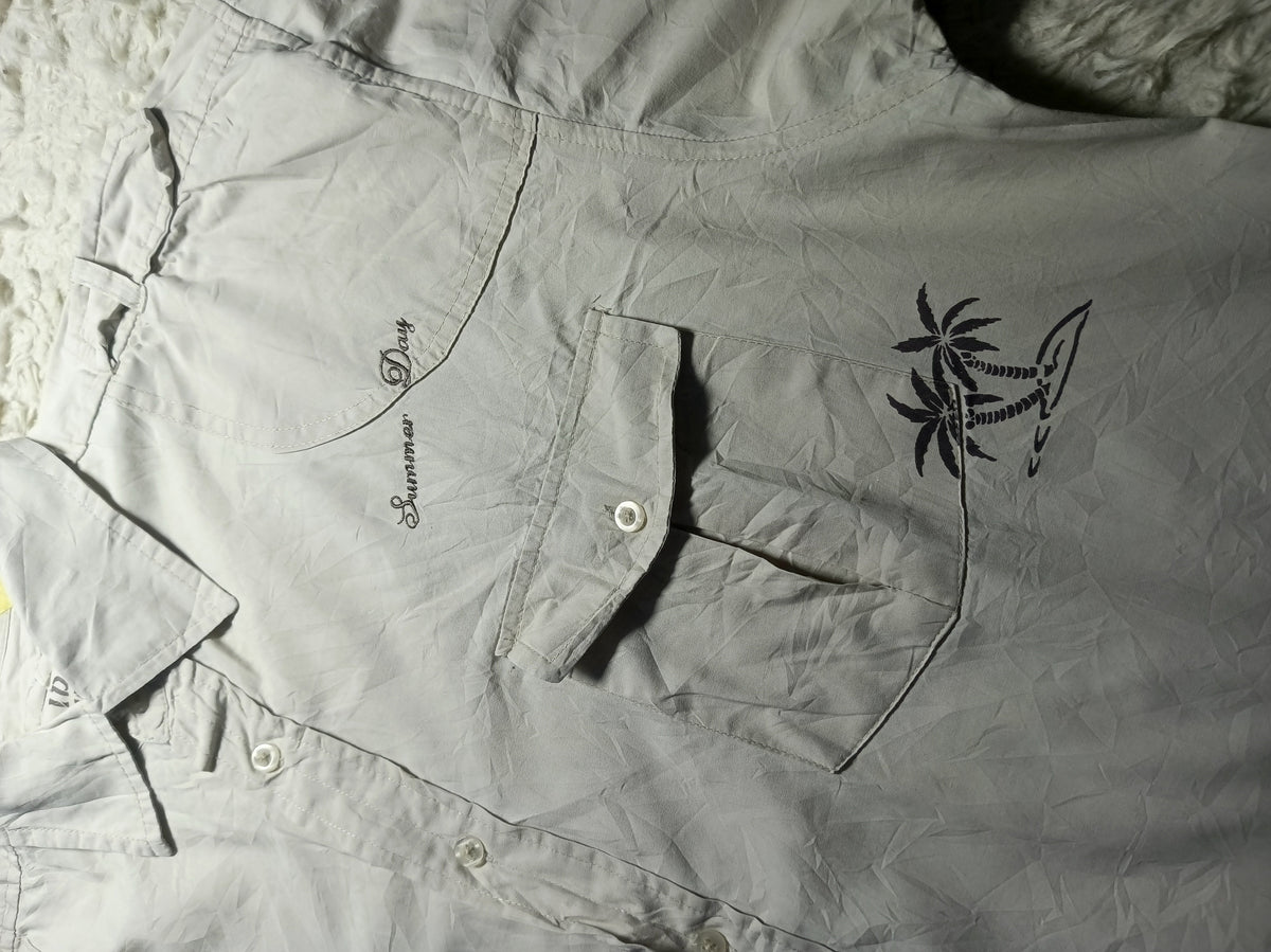 A light gray short-sleeve button-up shirt laid flat on a textured white surface, featuring a black palm tree and shark graphic on the chest pocket and 'Summer Vibes' text on the opposite side.