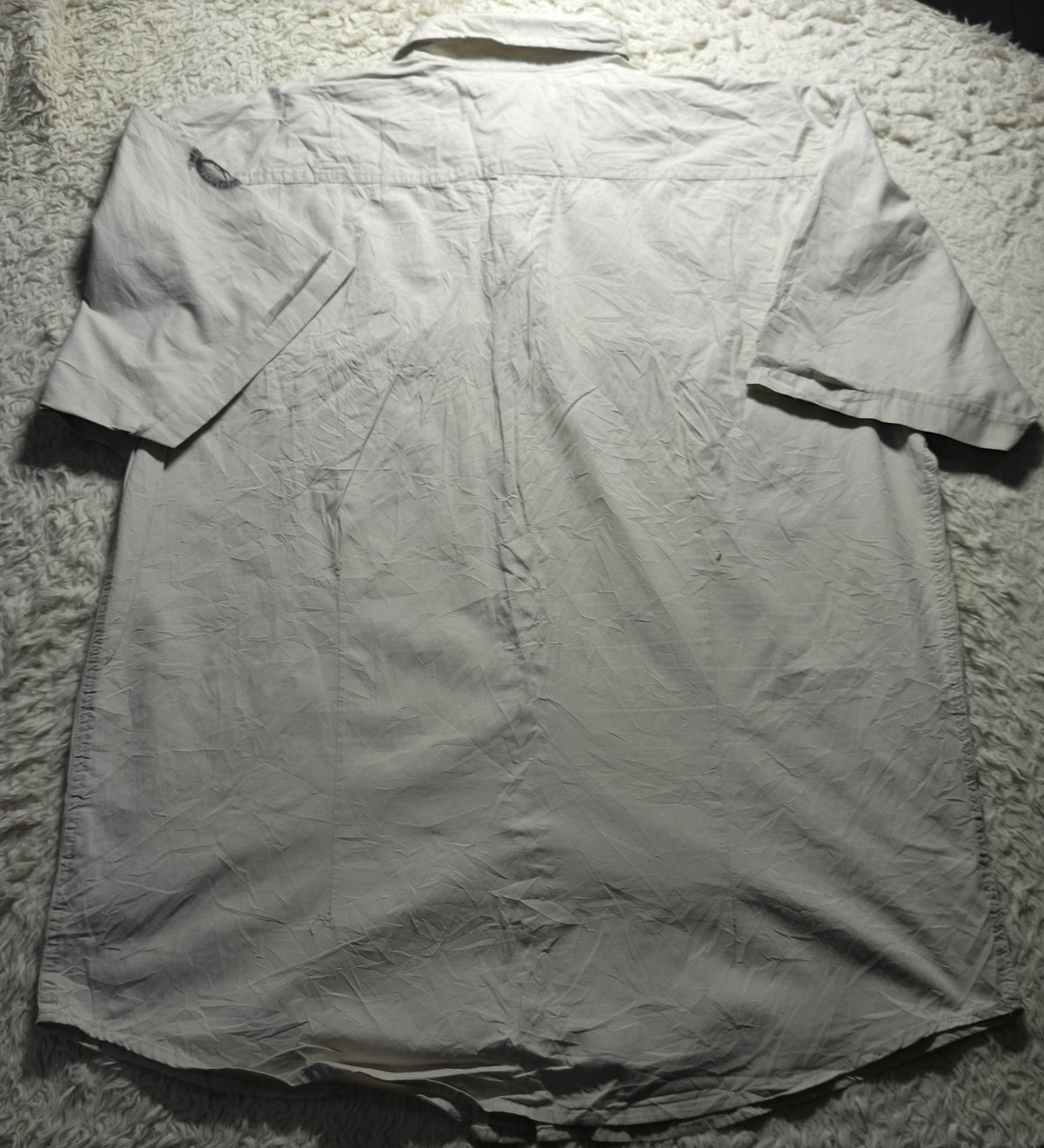 A light gray short-sleeve button-up shirt laid flat on a white shag rug, photographed from above.