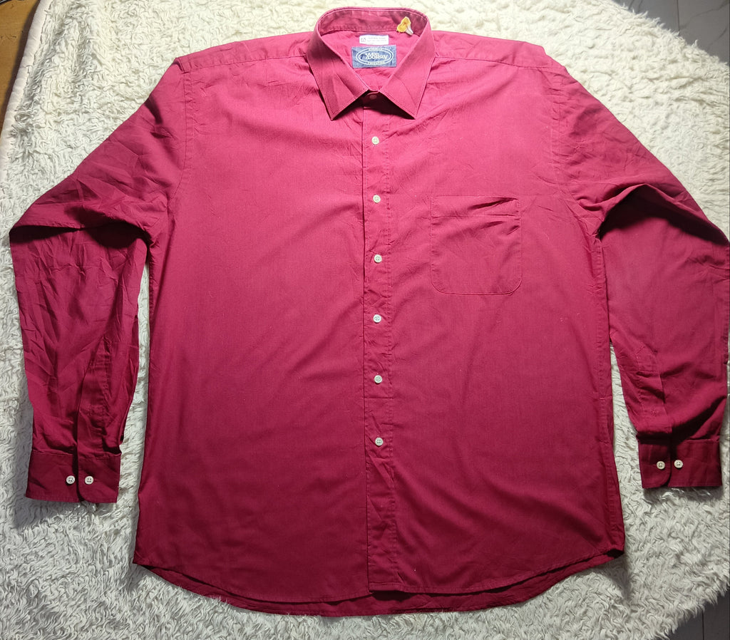 A long-sleeve button-up shirt in a deep magenta or burgundy red color, laid flat on a white faux fur blanket over a tiled floor.