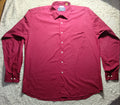 A long-sleeve button-up shirt in a deep magenta or burgundy red color, laid flat on a white faux fur blanket over a tiled floor.