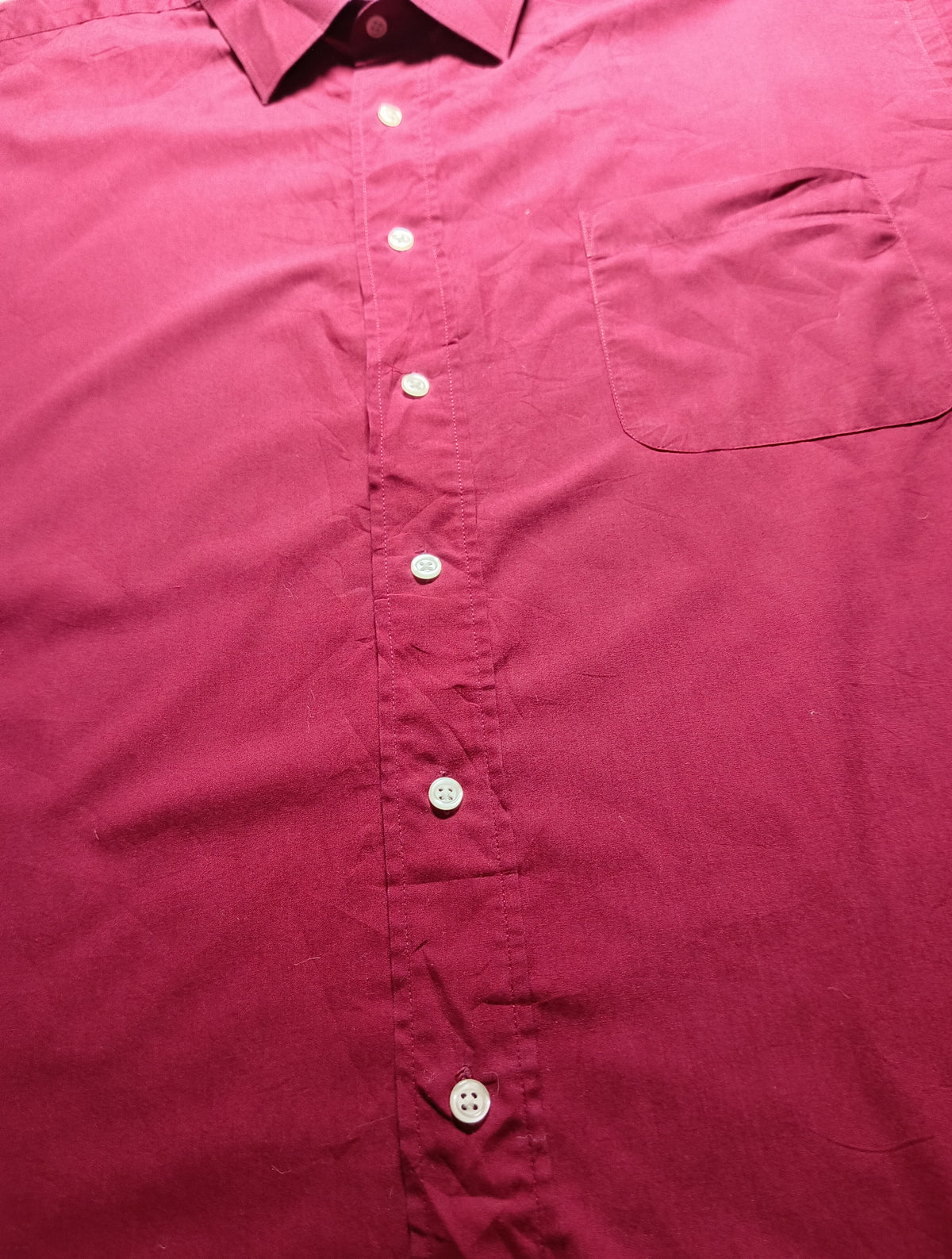 A close-up of a long-sleeve button-up shirt in a deep magenta or berry pink color, showing the front buttons, collar, and chest pocket.