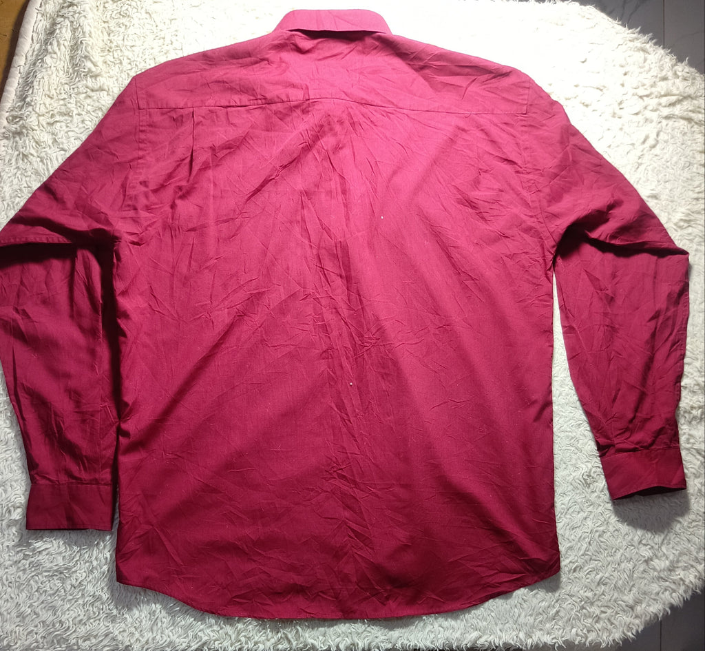 A long-sleeve collared button-up shirt in a solid magenta-pink color, laid flat on a white textured rug.