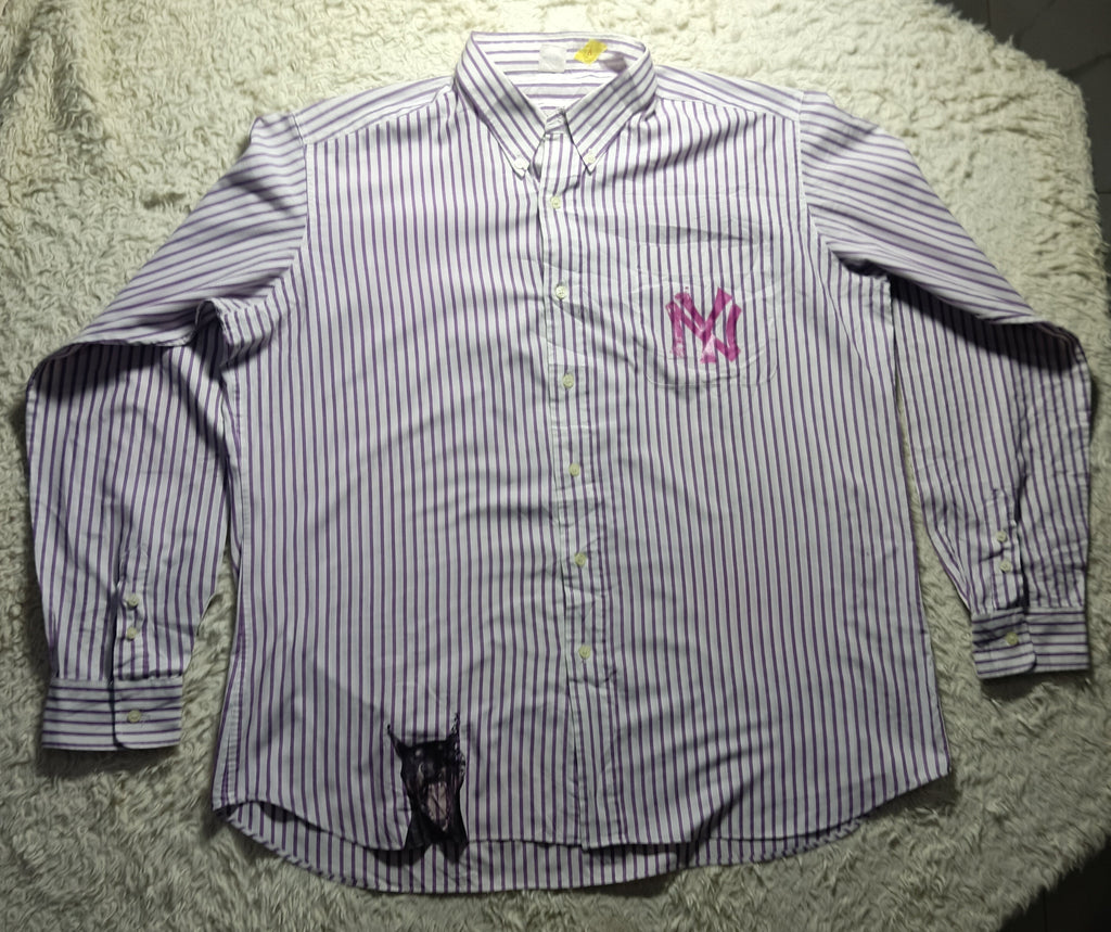 A long-sleeve button-up shirt with thin vertical purple and white stripes, featuring a pink embroidered 'NY' logo on the left chest and a black embroidered dog graphic near the bottom hem, laid flat on a white shag rug.