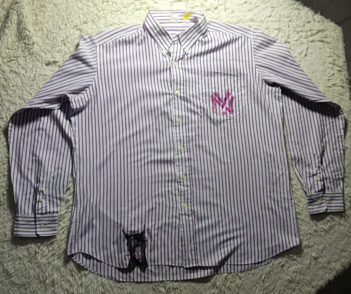 A long-sleeve button-up shirt with thin vertical purple and white stripes, featuring a pink embroidered 'NY' logo on the left chest and a black embroidered dog graphic near the bottom hem, laid flat on a white shag rug.