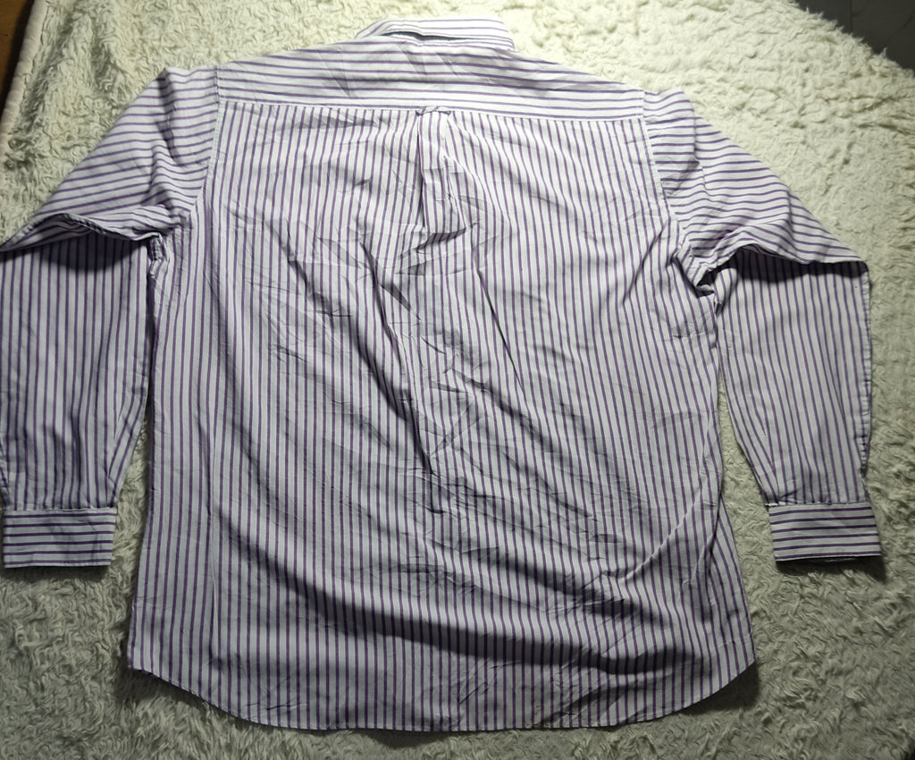 A long-sleeve button-up shirt with thin vertical blue and white stripes, laid flat on a white shaggy blanket.