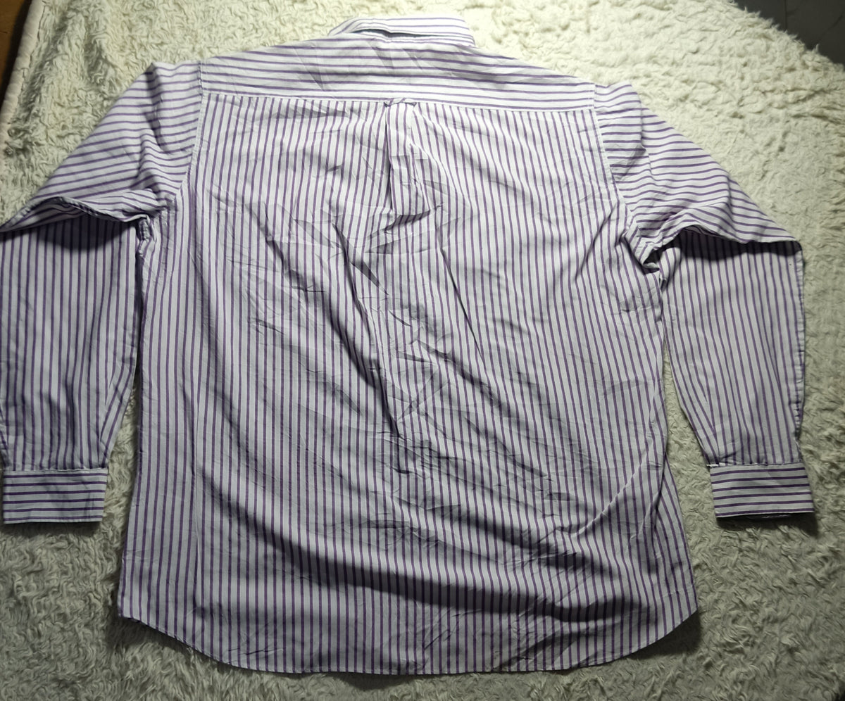 A long-sleeve button-up shirt with thin vertical blue and white stripes, laid flat on a white shaggy blanket.