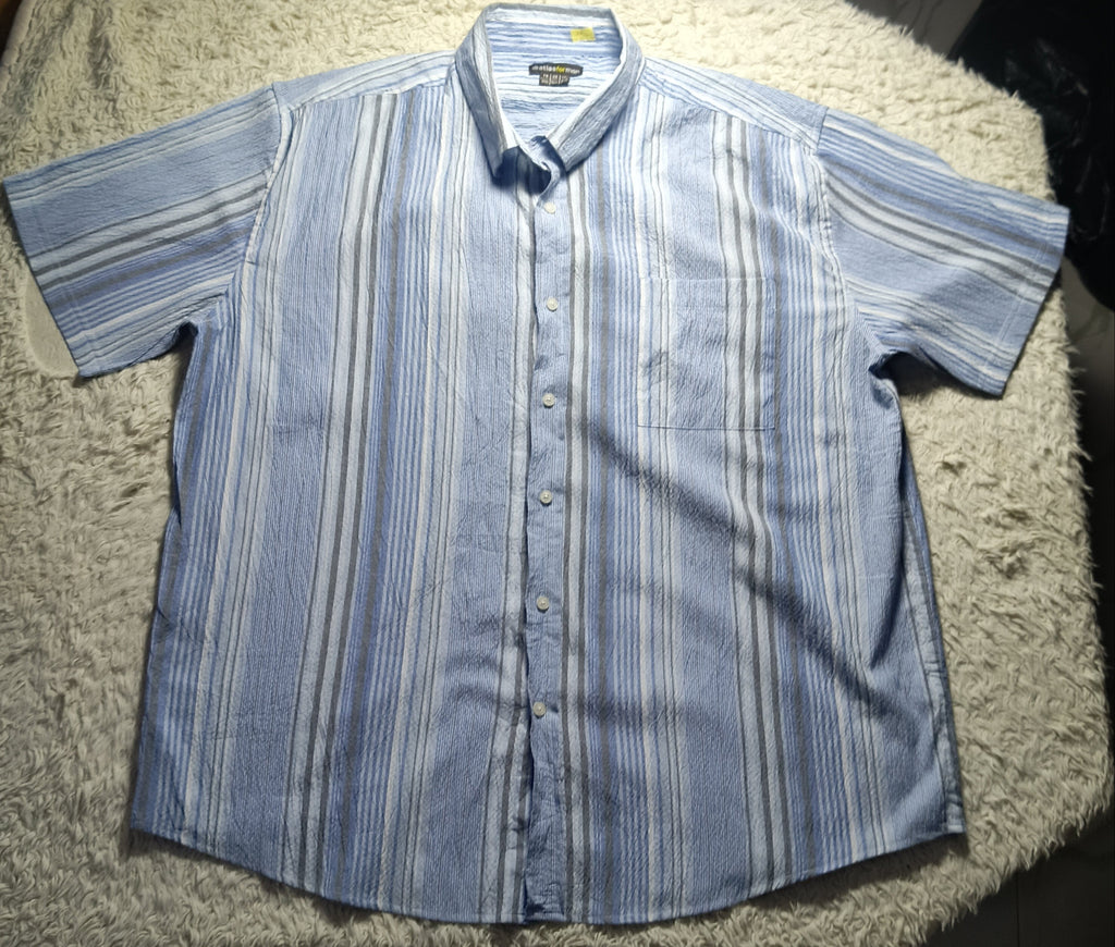 A short-sleeve button-up shirt with vertical blue, white, and gray stripes, laid flat on a shaggy cream rug.
