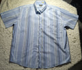 A short-sleeve button-up shirt with vertical blue, white, and gray stripes, laid flat on a shaggy cream rug.