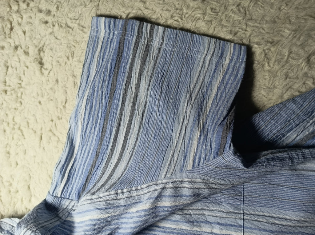 A close-up of a blue and white striped crinkled fabric, likely a shirt or jacket, laid flat on a textured beige rug. The image has a camera overlay at the bottom showing 'POVA 6 Neo' and '25mm f/1.