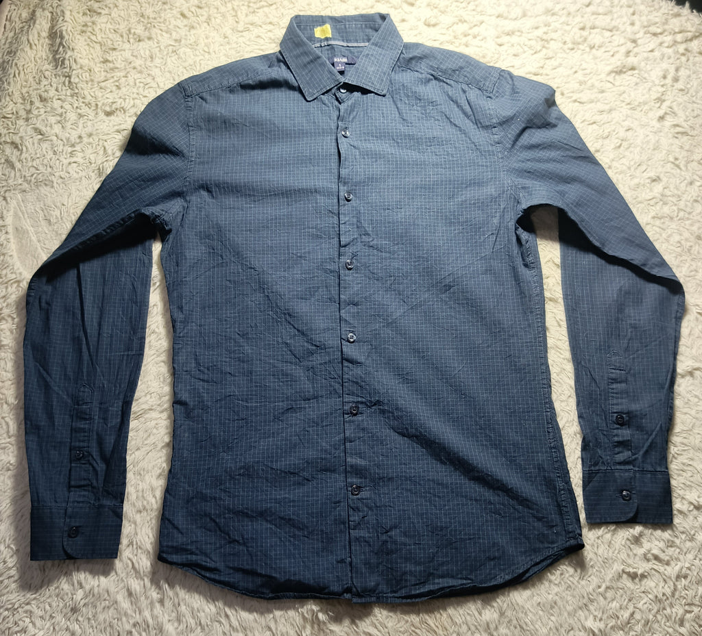 A long-sleeve button-up shirt in a dark blue textured fabric, laid flat on a white shag rug.