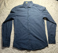 A long-sleeve button-up shirt in a dark blue textured fabric, laid flat on a white shag rug.