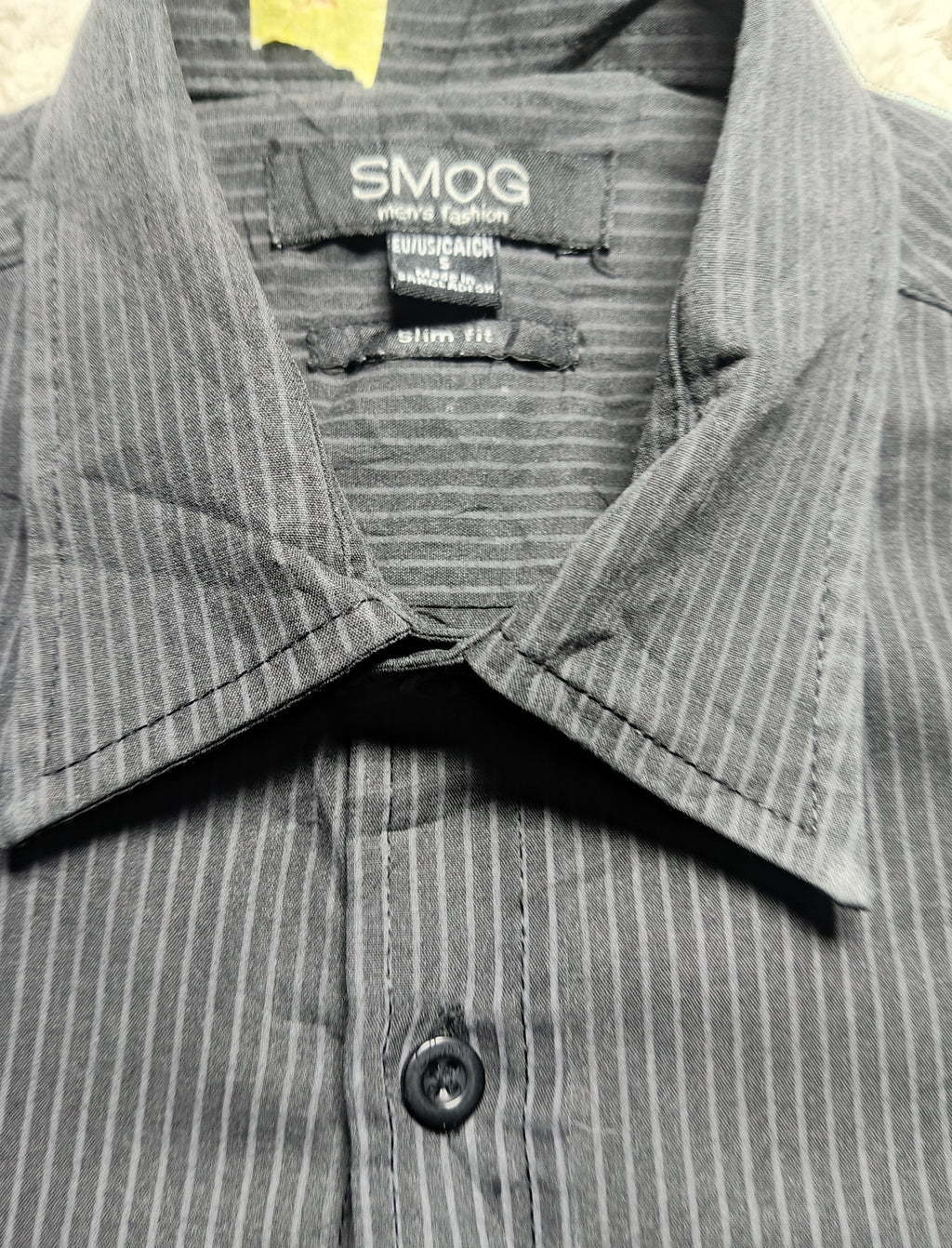 Close-up of a gray and black pinstriped button-down shirt collar with the brand label 'SMOG' visible inside the neck.