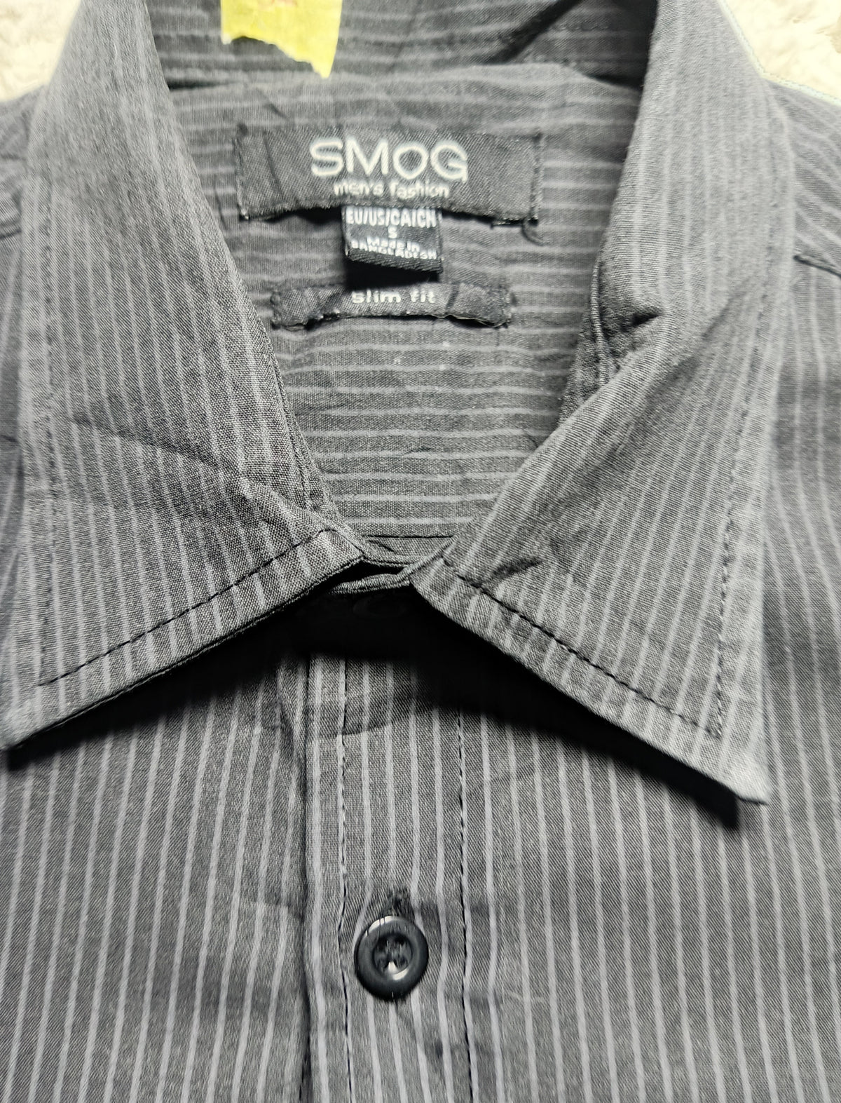 Close-up of a gray and black pinstriped button-down shirt collar with the brand label 'SMOG' visible inside the neck.