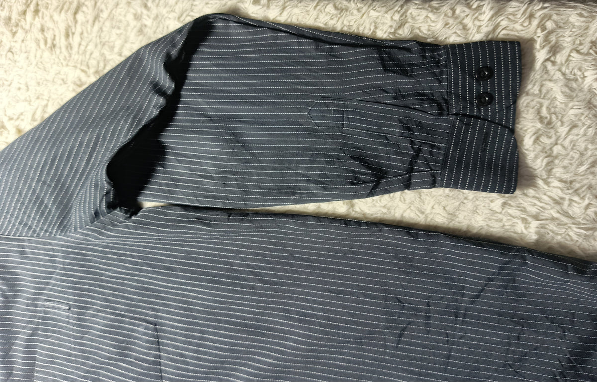 A pair of dark gray and white pinstriped trousers laid flat on a white shag rug, showing the fabric texture and a buttoned cuff.