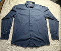 A dark blue long-sleeve button-up shirt laid flat on a white shag rug, with a light box and other items visible in the background.
